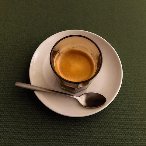 An espresso in a glass on a white saucer, on deep green