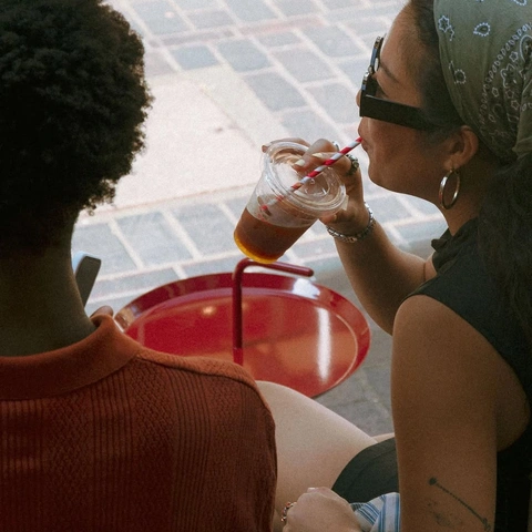 Two friends with iced coffees at a red cafe table
